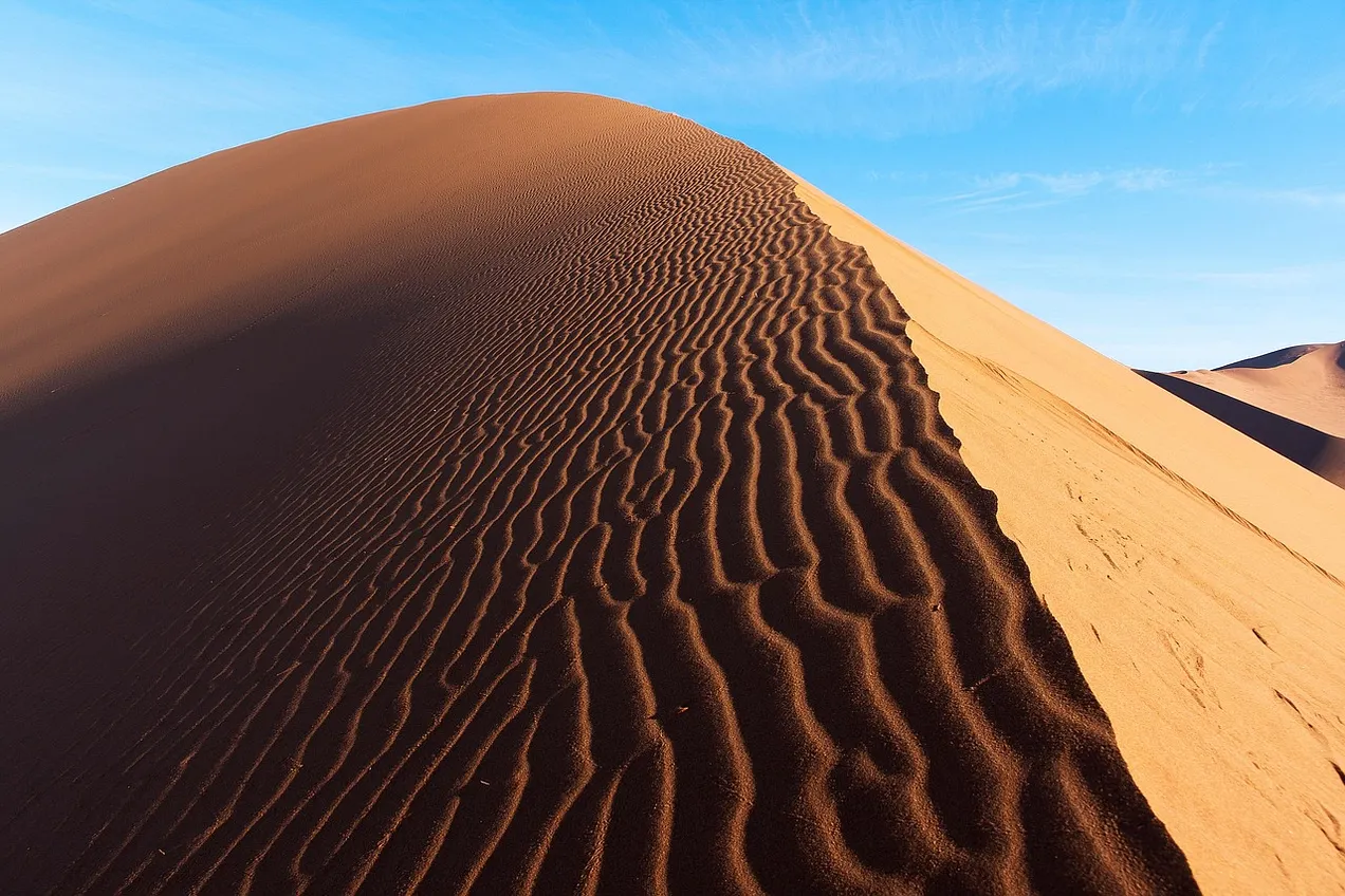 A photo of the Namibia desert sand with a rusty, shaded part on the left and a lighter color sloping down on the right.
